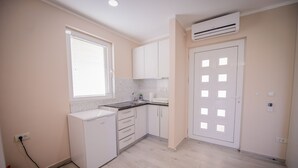 A compact kitchen with white cabinets, a built-in dishwasher, a window with blinds, and a door with a square pattern.