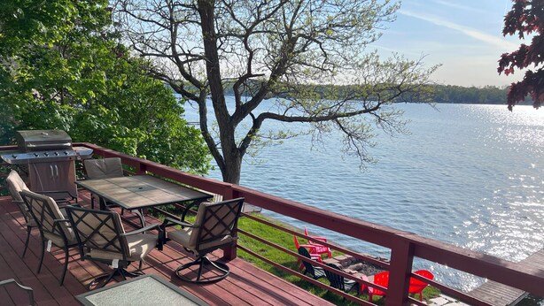 A wooden deck with outdoor furniture, a grill, and a view of a lake.