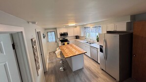A compact kitchen with a central island, stainless steel appliances, and a window with a curtain.