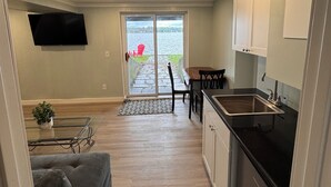 A compact living space with a kitchenette, a dining area with a table and chairs, a sofa, and a TV mounted on the wall.