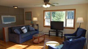 A living room with a sofa, armchair, TV, and a ceiling fan.