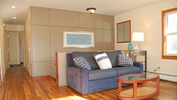 A living room with a blue sofa, a glass coffee table, and a wooden floor.