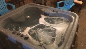 A hot tub with two people in it, surrounded by blue Adirondack chairs and a wooden table.