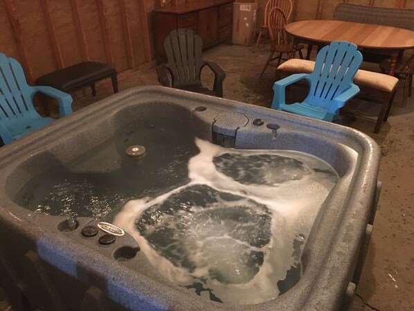 Un jacuzzi con dos personas adentro, rodeado de sillones Adirondack azules y una mesa de madera.