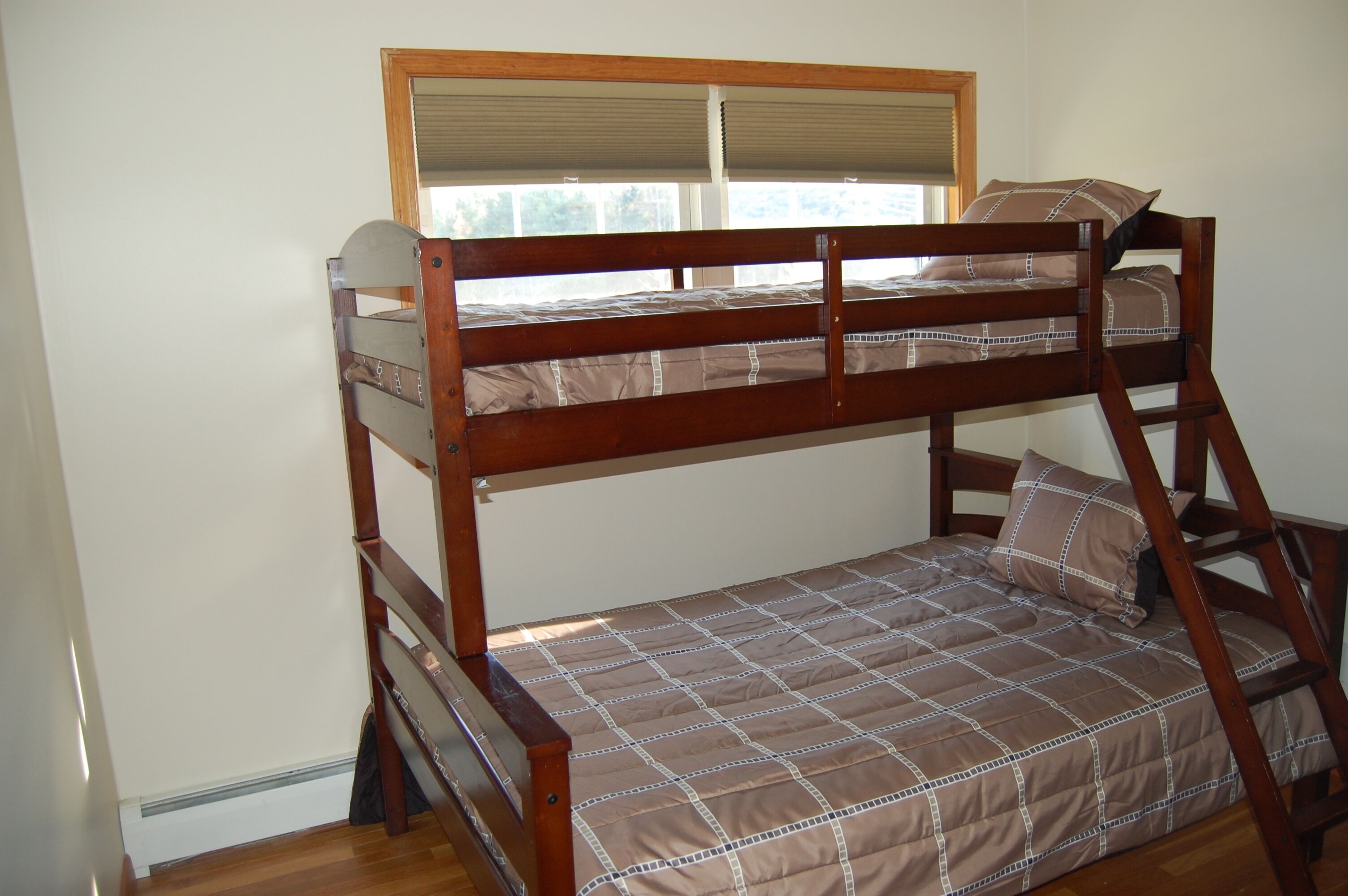 A bunk bed with a wooden frame, a window with blinds, and a checkered bedspread.