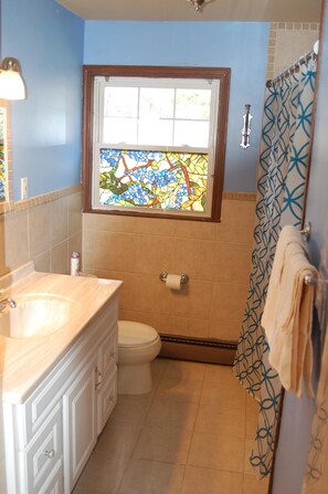 Un baño con inodoro, lavamanos y ventanal con diseño de vitral.