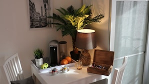Una mesa bien ordenada con una lámpara, una planta en maceta, una bandeja de frutas y una pequeña caja de gafas de sol.