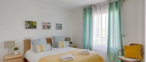 Ein Schlafzimmer mit einem Bett, Nachttischen, einem Sessel und Vorhängen.