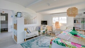Una sala de estar moderna con un sofá, una mesa de centro y un televisor. Hay una estantería y una ventana con persianas.