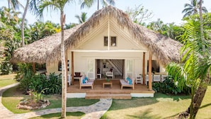 A thatched-roof bungalow with a covered outdoor seating area and a staircase leading to the entrance.