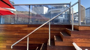 Une terrasse en bois avec des garde-corps en verre et des rampes en métal.