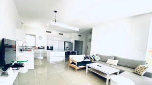 Un salon moderne avec un canapé gris, une table basse blanche et un téléviseur posé sur un meuble.