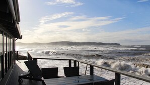 A deck with two chairs and a table overlooking a turbulent sea with waves crashing onto the shore. - 'Seabreeze' a unique Waterfront/Beachside property (Pearl Beach)