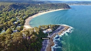 Une vue aérienne de Seabreeze, montrant une propriété située en bord de mer, avec une grande maison, une forêt dense environnante et une vue dégagée sur l’océan.