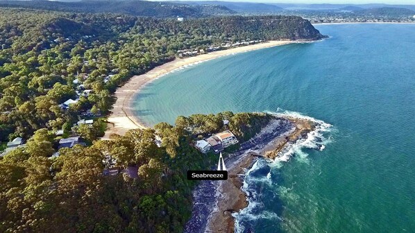 An aerial view of Seabreeze, featuring a beachfront property with a large house, dense surrounding forest, and a clear view of the ocean. - 'Seabreeze' a unique Waterfront/Beachside property (Pearl Beach)