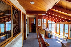 Interior de cabana com decoração em madeira, grandes janelas, um banco e uma área de cozinha.