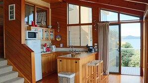 Une cuisine avec des meubles de rangement en bois, un four à micro-ondes et un évier. On y trouve des tabourets et un panier sur le comptoir.