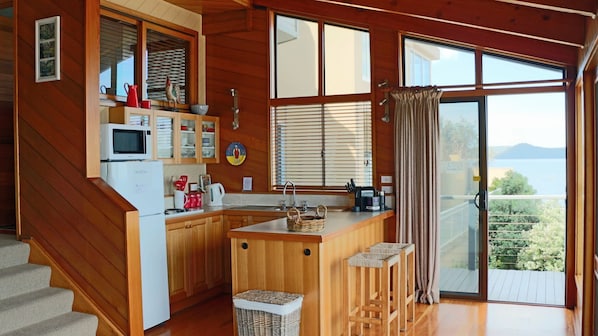 A kitchen with wooden cabinets, a microwave, and a sink. There are stools and a basket on the counter. - 'Seabreeze' a unique Waterfront/Beachside property (Pearl Beach)