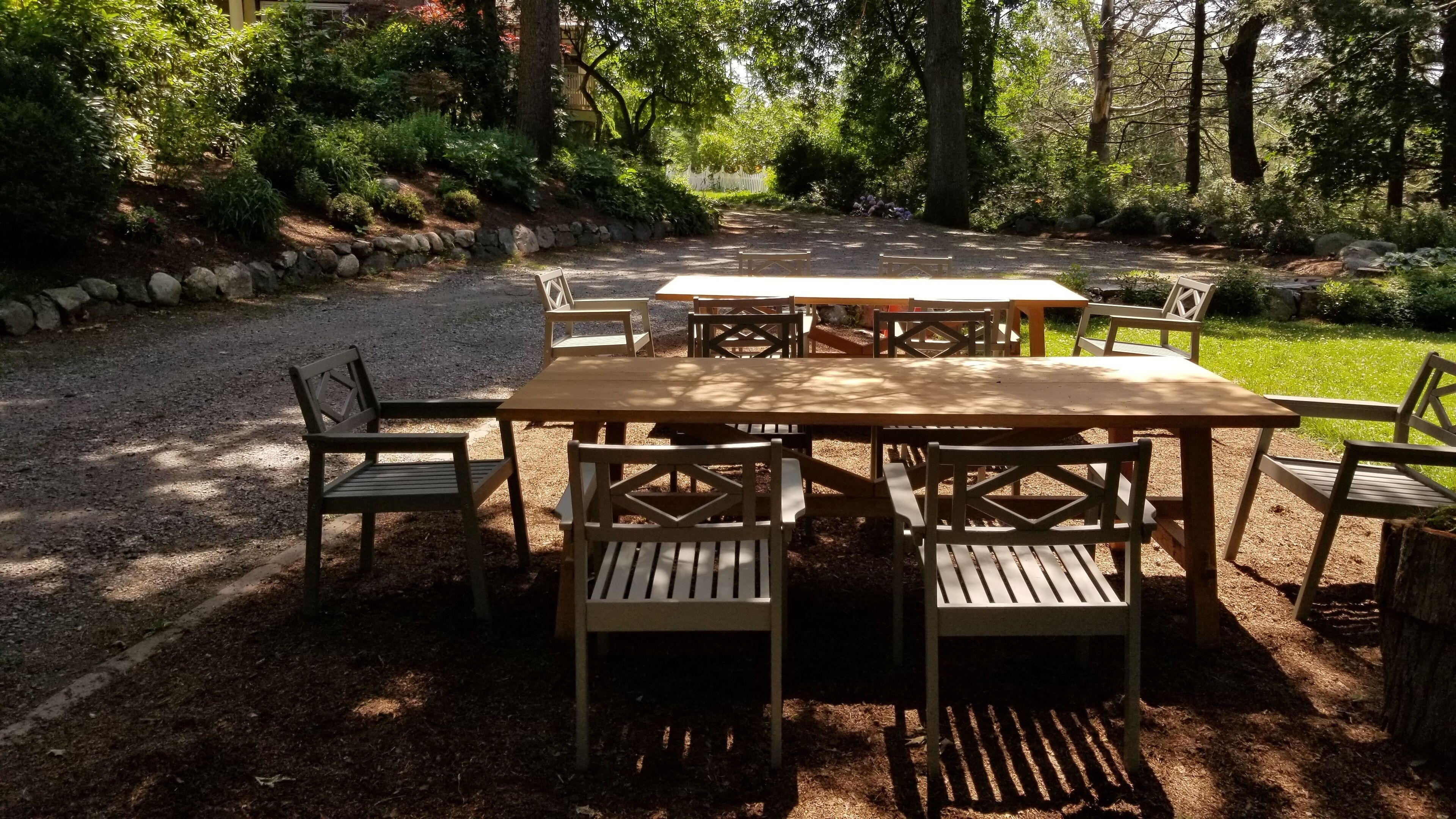 Un espace de restauration en plein air, avec des tables et des chaises en bois, entouré d’un chemin de gravier et d’une végétation luxuriante.
