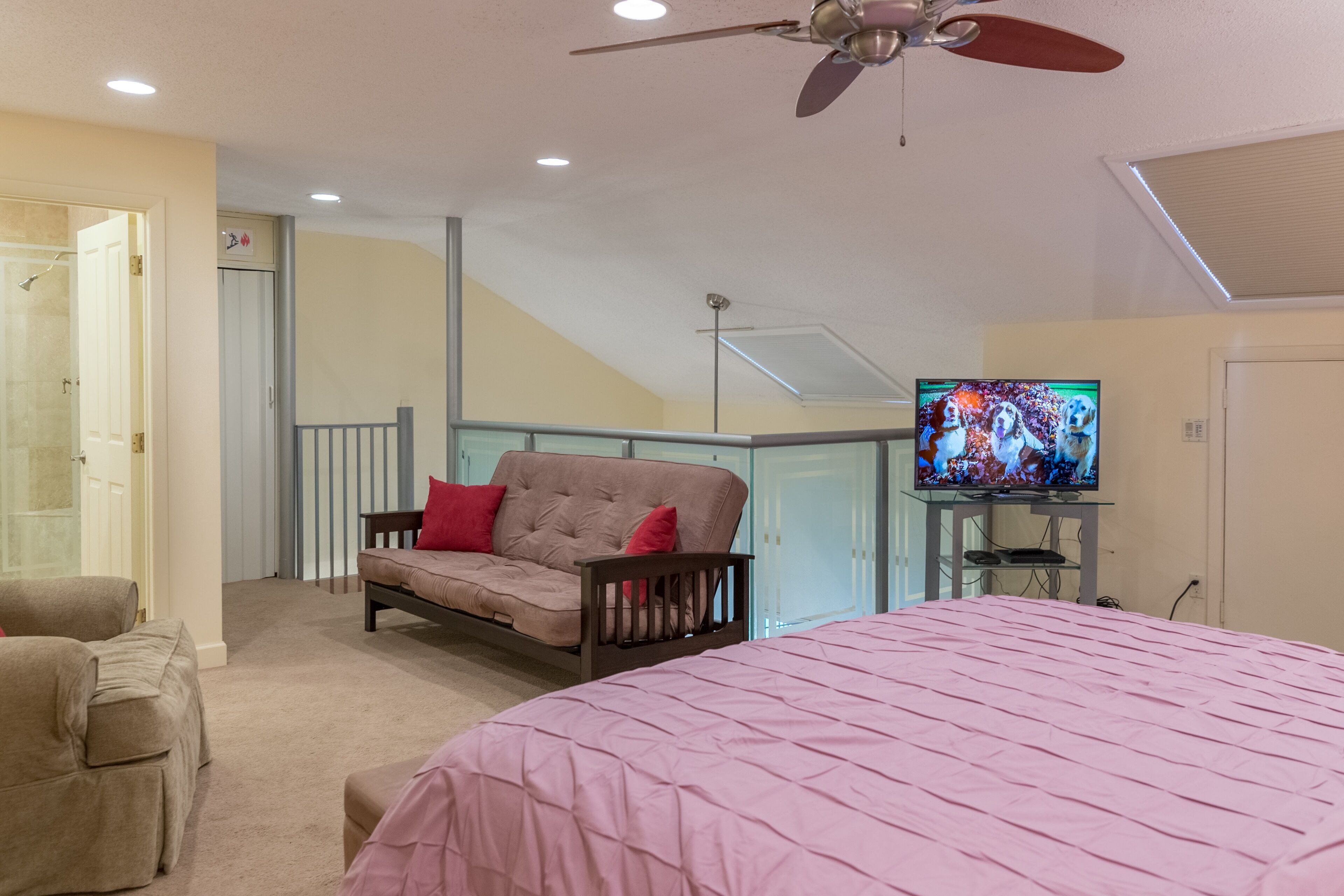 A bedroom with a bed, a sofa, a television, and a ceiling fan.