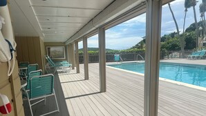 Une terrasse couverte avec une piscine, des chaises vertes et une vue sur l’océan.