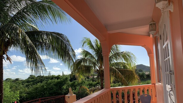 Ein Balkon mit Blick auf üppige Vegetation und Palmen, einem Geländer und zwei Stühlen.