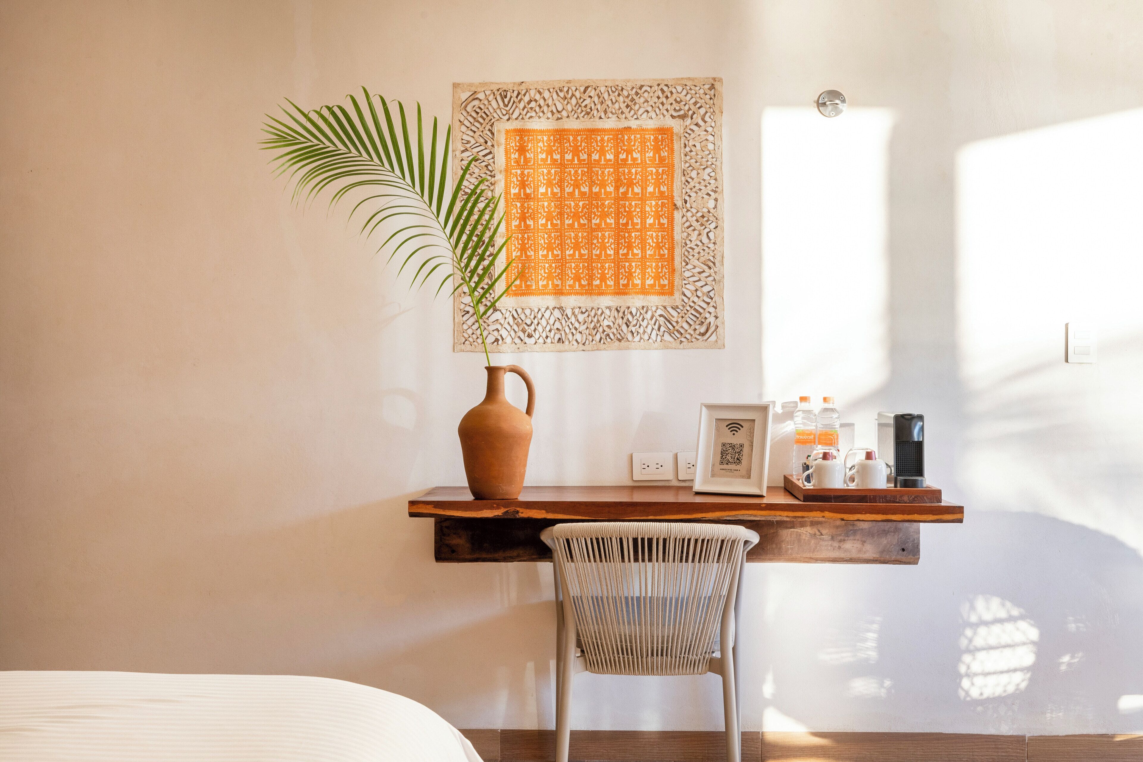 Una habitación con una cama, un escritorio con un florero, un cuadro enmarcado y una silla.