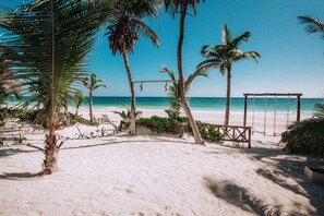 A beach with a swing set and palm trees.