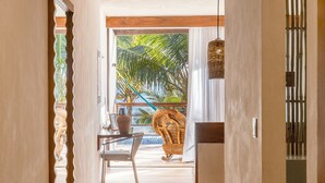 A hallway with a wooden floor, a dining area with a table and chairs, and a view of palm trees through a window. - Hotel Los Arrecifes (Tulum)