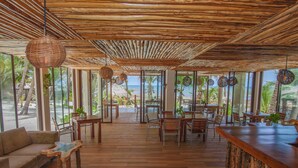A spacious indoor area with wooden flooring, a wooden ceiling, and large windows offering a view of the beach. - Hotel Los Arrecifes (Tulum)