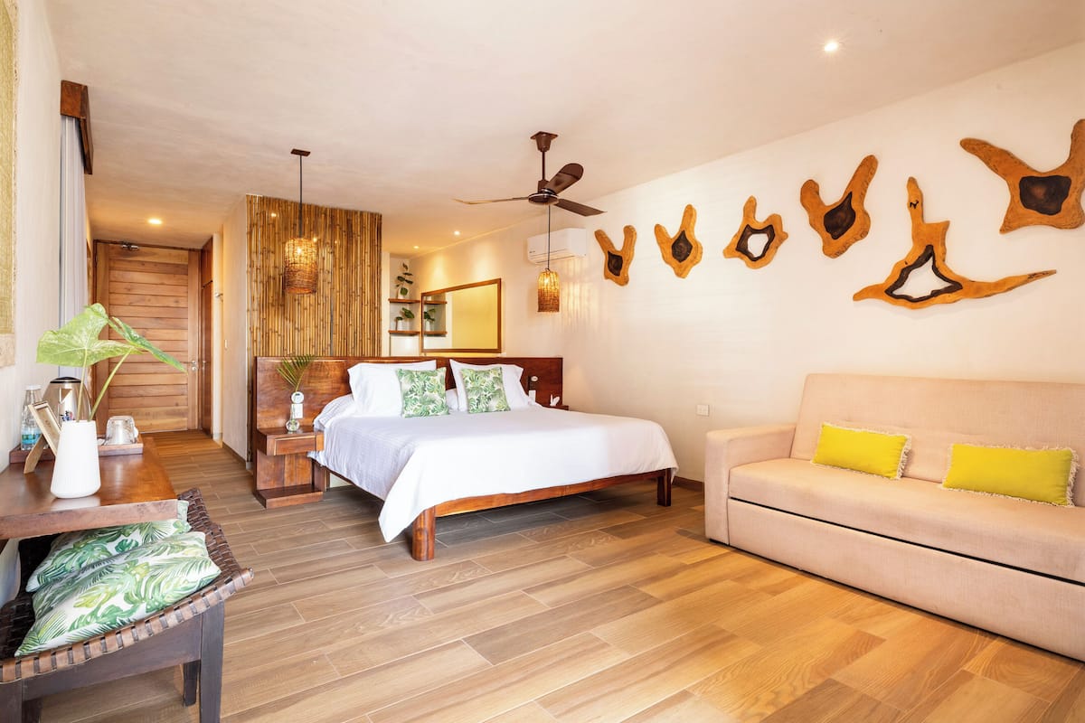 Un dormitorio moderno con suelo de madera, cama con ropa de cama blanca, sofá beige con cojines amarillos y decoraciones en forma de animales montadas en la pared.