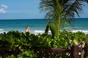 A beach scene with a person in the water, palm trees, and ocean waves. - Hotel Los Arrecifes (Tulum)