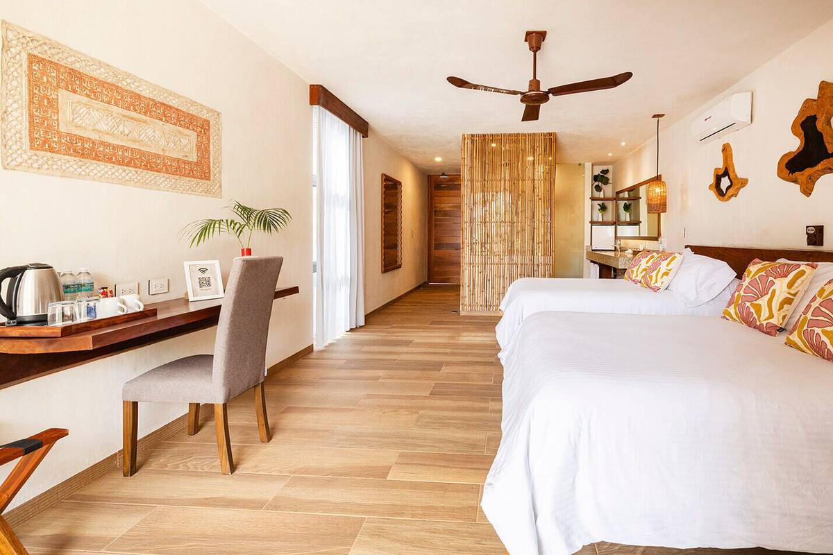 Habitación de hotel con escritorio, dos camas, ventilador de techo y ventana grande.