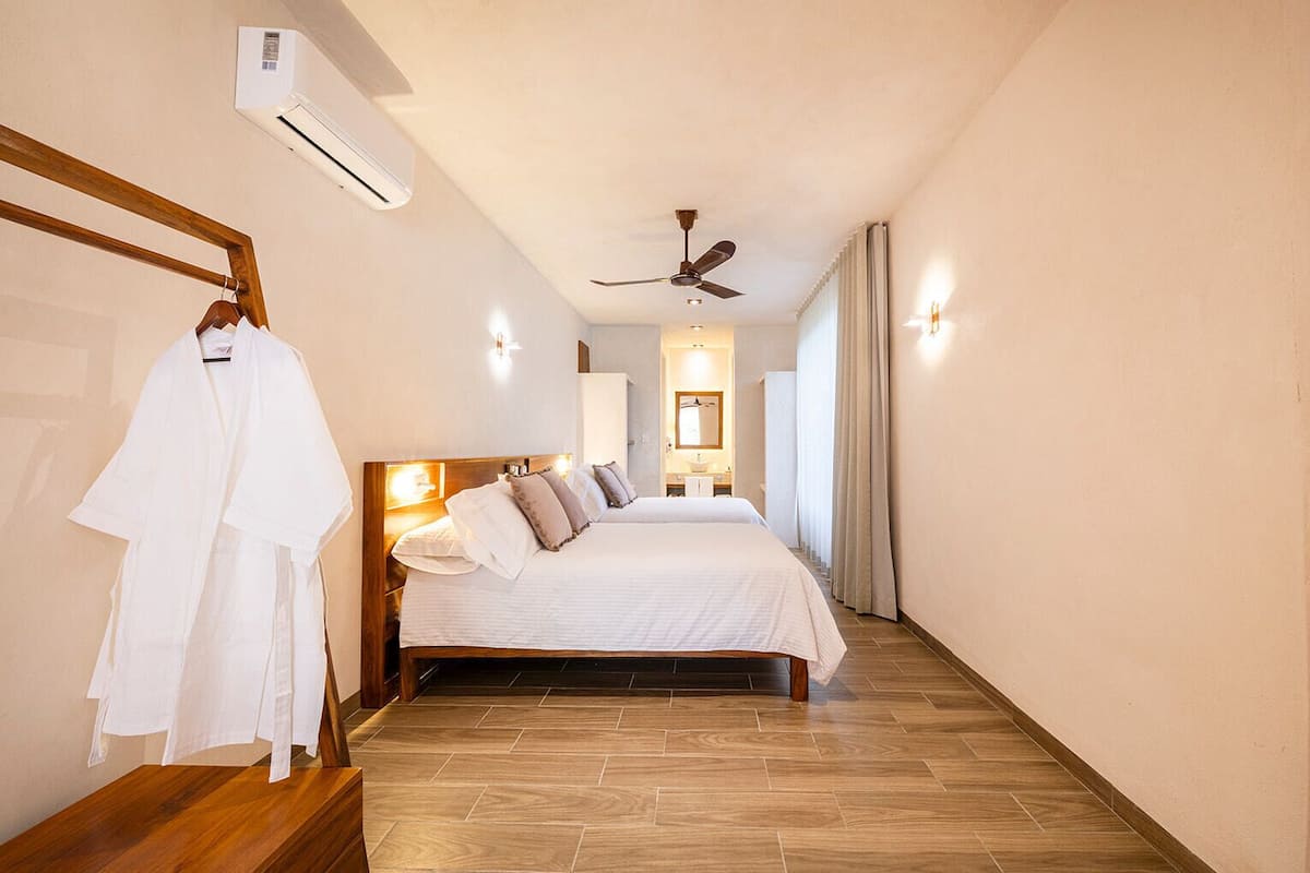 Habitación de hotel con cama, cabecero de madera, ventilador de techo y aire acondicionado de pared.