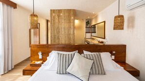 A hotel room with a large bed, wooden headboard, two bedside tables, a nightstand, a mirror, and a hanging light fixture. - Hotel Los Arrecifes (Tulum)