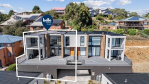 Una casa moderna de dos pisos con balcón, ventanas grandes y techo plano.
