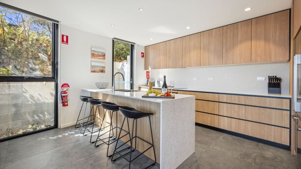 Una cocina moderna con una isla central, taburetes de bar, armarios de madera y un ventanal grande.