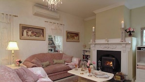 A cozy living room with a fireplace, a sofa, a coffee table, and a bookshelf. - Jasmine's Cottage Barossa Valley Vineyard Views (Barossa Valley)