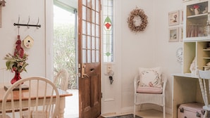 A cozy room with a wooden door, a wicker chair, a small table, and a white bench. - Jasmine's Cottage Barossa Valley Vineyard Views (Barossa Valley)