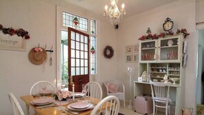 A dining area with a wooden table set for four, white chairs, a chandelier, a green cabinet with glassware, and a wall clock. - Jasmine's Cottage Barossa Valley Vineyard Views (Barossa Valley)