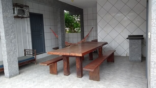 Un amplio patio con una gran mesa de madera y bancos, una hamaca y un pilar de piedra.