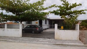 Una propiedad cerrada con un coche estacionado adelante, un edificio con un letrero y un árbol que da sombra.