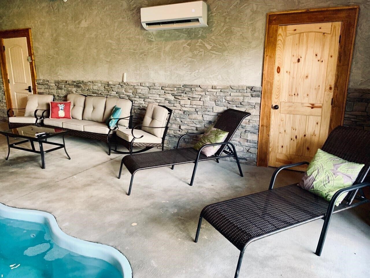 A covered outdoor seating area with a stone wall, a pool, and a wooden door.