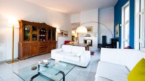 Un salon avec un canapé blanc, une table basse en verre, un meuble en bois et une cheminée.