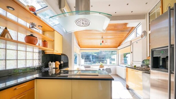 Une cuisine moderne dotée d’un îlot central, d’appareils électroménagers intégrés et d’un plafond en verre.