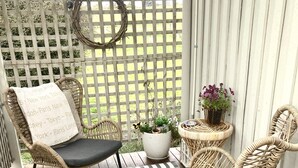 Un patio couvert aménagé avec des fauteuils en osier, un tapis à motifs, des plantes en pot et une guirlande décorative.