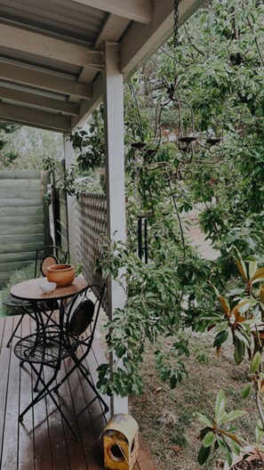 A covered patio with a round table and chairs, surrounded by lush greenery and a hanging plant. - White Croft country cottage (Ross)