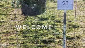 Un espace délimité par une clôture, avec un panneau d’accueil, un panneau indiquant le numéro de l’endroit, et un petit bâtiment en arrière-plan.