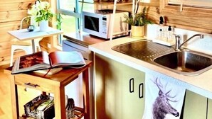 Une cuisine de taille réduite avec des murs en bois, un four à micro-ondes, un évier et une fenêtre équipée de stores.