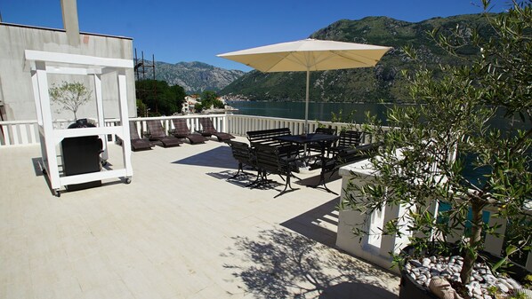 An outdoor patio with a grill, lounge chairs, and a table with an umbrella.